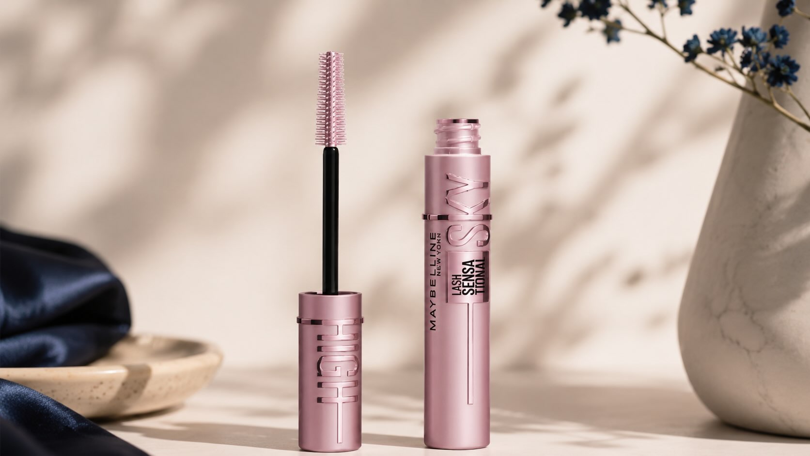 Maybelline Sky High Mascara tube with wand on cream background