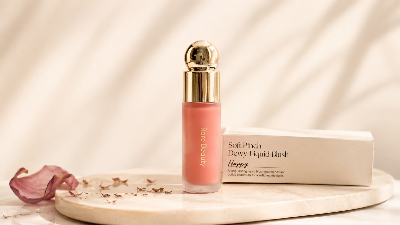 Rare Beauty Soft Pinch Liquid Blush bottle with rose petal on cream background